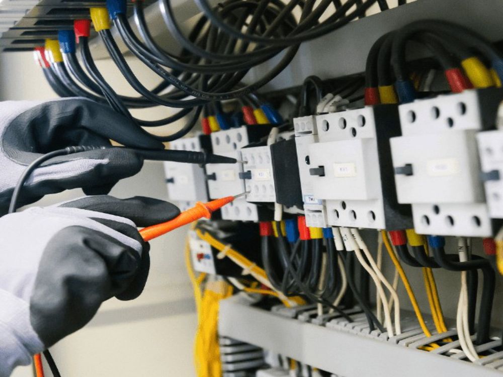 Sample image: gloved hands testing an electrical panel with probes